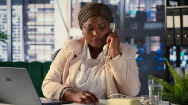 Afrika kökenli Amerikalı yönetmen, mali değerlendirme için sabit telefon görüşmesini kullanıyor. Kadın CEO kaynak tahsisi, bütçe planlaması ve son teslim tarihi yönetimi, karar verme konularını tartışıyor. Kamera A.