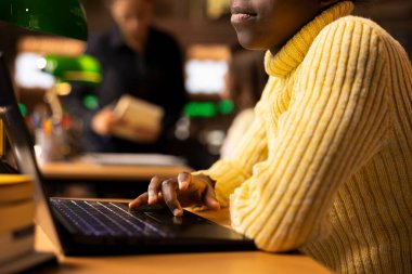 Afrikalı Amerikalı liseli kız kütüphanedeki bir çalışma masasında ders notları yazıyor, bir okul projesi üzerinde bilgisayarında online bilgi ile sıkı çalışıyor. Öğrenci akademik enstitüde ders için hazırlanıyor.