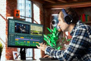 Ham görüntüleri parlatmak ve ses kalitesini arttırmak için ev ofisinde kulaklık takan bağımsız video editörü. Videograf klipleri profesyonel olarak ayarlıyor, filme ses efektleri uyguluyor