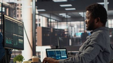 Ofiste kollarını ve sırt kaslarını esneten Afrikalı Amerikalı bir çalışan idari bir görevi bitirdikten sonra sandalyesinde dinleniyor. Erkek analist şirket için hedefler belirliyor. Kamera A.