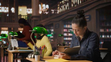 Kitap okuyan ve notlarını tamamlamak, özel dersleri için doğru öğrenme materyalleri yaratmak ve akademik bir ortamda akıl hocalığı yapmak için kısa bir özet hazırlayan bir kadın öğretmen. Kamera A.