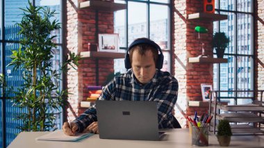 Müzik dinleyen işçiler, masadaki bilgisayardaki verileri analiz eden, analitik raporları derleyen. İşçi kulaklık takıyor, defter cihazı kullanıyor, bilgi yazıyor, kamera A