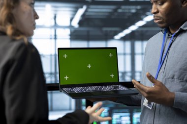 Veri merkezindeki ekip çalışanları yeşil ekran model dizüstü bilgisayarda otomasyon araçları kullanıyorlar. Sunucu çiftliğinin sürekli güncellenmesini sağlayan mühendisler, krom anahtar aygıtı ile veri akışını yönetirler