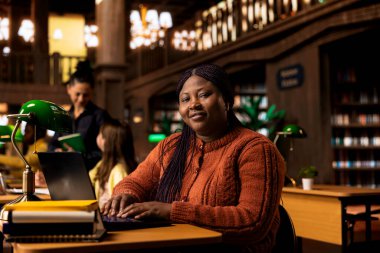 Notlarını inceleyen ve kütüphane masasında ders hazırlayan kendinden emin bir öğretmenin portresi pedagoji ve akıl hocalığına olan bağlılığını gözler önüne seriyor. Öğrencilerine akademik destek sağlıyor..