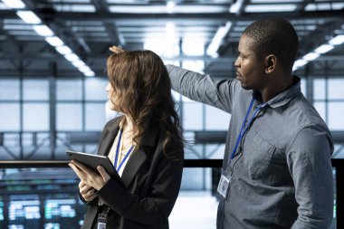 Tablet tutan iş arkadaşları, veri merkezine bakıyorlar, sunucuların sanal hale getirilmesini yönetiyorlar. Sunucu odası çalışanları ağ protokollerini inceliyor, gelişmiş güvenlik önlemleri uyguluyor