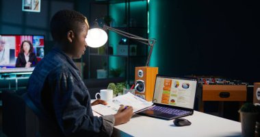 Kişisel ofiste çalışan serbest çalışan bir kadın dizüstü bilgisayardaki istatistiksel veri finans grafiklerini kontrol ediyor. Uzaktan kumandalı çalışan oturma odasında iş dünyasının grafiksel rakamlarını karşılaştırıyor, kamera B