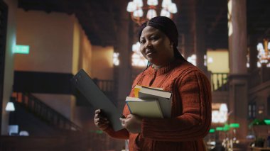 Kadın eğitimci kütüphanede öğretmenlik materyallerini ve kaynaklarını hazırlıyor, uzmanlığını akademisyenlere danışmanlık yapmak ve genç zihinler için üretken bir akademik atmosfer yaratmak için kullanıyor. Kamera A.