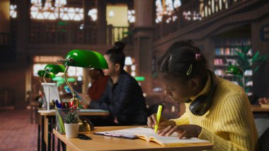 Öğrenme oturumunda anahtar sözcükleri ve cümleleri vurgulamak için floresan kalem kullanan Afrikalı Amerikalı öğrenci önemli ders notlarını işaretleyip altını çiziyor. Bilgin sınavlara hazırlanıyor. Kamera A.