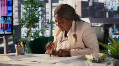 Siyahi şirket sahibi yeni bir ofis için mimari taslaklar hazırlıyor, başlangıç merkezinin yerini değiştirmek istiyor. Yaratıcı bir çalışma alanı tasarlamak için müteahhitlerle işbirliği yapıyor. Kamera A.