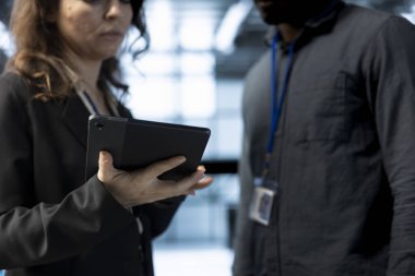 Teamworking colleagues in data center using tablet, analyzing metrics, optimizing storage volumes. Close up of server room workers using device, reviewing network paths, ensuring seamless operations clipart