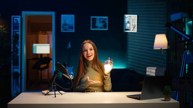 İçerik yaratıcısı stüdyoda ampulü sunuyor, profesyonel ekipmanlarla çekim yapıyor. Genç kız apartmanda pazarlama yapıyor, ışıklandırma ekipmanları, kamera B