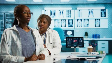 Afrika kökenli Amerikalı kadın doktor steteskopla solunum danışmanlığı yapıyor. Kalp atışlarını ve akciğerlerinin normal çalışmasını dinliyor. Doktor genç hastasının nabzını kontrol ediyor. Kamera B.