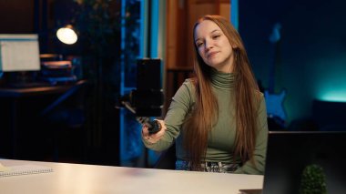 Apartman dairesinde internet yayın kanalı için selfie çubuğuyla telefon kullanan neşeli genç filmleri. Gülümseyen gen z etkileyicisi abonelerle etkileşime girer, telefonla kayıt yapar, kamera A