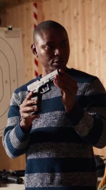 Dikey video atış menzili güvenlik görevlisi müşterilerin kurallara uymalarını ve silahlarını güvenli bir şekilde kullanmalarını sağlıyor. Afrikalı Amerikalı atış poligonu çalışanı müşterilere talimat veriyor.