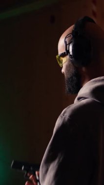 Dikey video atış menzilli müşteri tabancayla hedefleri vuruyor, yakın mesafeden silah kullanmayı öğreniyor. Kapalı alanda ateş eden, ölümcül ateş eden, koruyucu takan bir adam var.