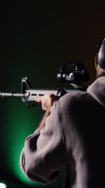 Dikey video atış menzili müşterisi yarı otomatik silahla hedefleri vuruyor, eğleniyor. Kapalı alanda ateş eden bir adam, av tüfeği kullanıyor, koruma ekipmanı takıyor.