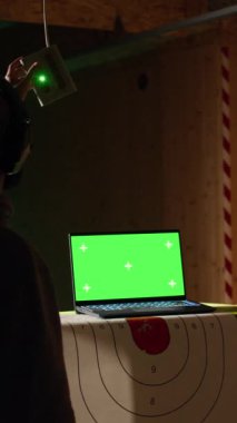 Dikey video yeşil ekran dizüstü bilgisayar, atış poligonundaki güvenlik görevlisinin yanında müşterinin hedeflere ateş edişini izliyor, onu denetliyor. Sahte defter ve atış poligonu uzmanı insanlara silah kullanmayı öğretiyor.
