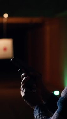 Mutlu atış poligonunun dikey video portresi. Müşteri silah dolduruyor, hedef vuruyor, eğleniyor. Zemin kattaki tesiste neşeli bir adama yaklaşın. Silah doldurun, koruyucu gözlük takın.