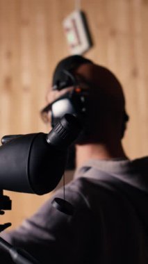 Dikey video atış aralığı müşterisi yakınlaştırma cihazına bakıyor. Eğitmen gözetmeninin yanında hedef tahtası kurup kurmadığını kontrol etmek için. Ateşli silah kullanırken mercek kullanılarak çekilen hedefleri analiz eden kişi