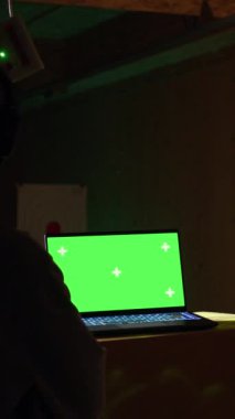 Atış menzilinde, hedefleri başarılı bir şekilde vuran adamın yanındaki dikey video yeşil ekran laptop. Eğitmen tarafından hedef tahtası, kamera ve kameraya isabet ettirdiği için tebrik edilen kişinin yanındaki maket defteri.