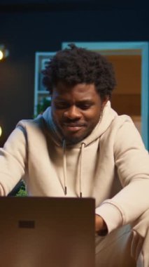 Dikey Video Odaklı Adam evde bir iş projesi için çevrimiçi araştırma yapıyor, kahve masasında dizüstü bilgisayarla oturuyor ve internette makaleler okuyor. Web sayfalarında gezinen ve toplanan kişi