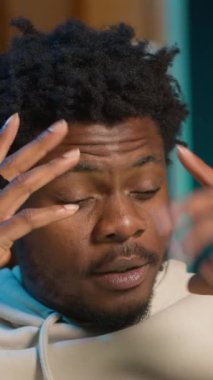 Dikey Afrikalı Amerikalı adam migren ve hastalıktan muzdarip, evinde kanepede oturuyor ve kendini çok yorgun hissediyor. Endişeli genç yetişkin acıyla boğuşuyor, yorgun ve endişeli adam. Kamera B.