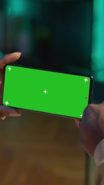 Dikey Video Afrikalı Amerikalı, modern moda evinden kalma yeşil ekranlı bir cihaz kullanıyor, kanepede oturuyor ve oturma odasında çalışıyor. Kendinden emin mutlu genç adam. Kamera.