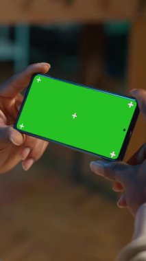 Dikey Afrikalı Amerikalı genç yetişkin, o kanepede dinlenirken oturma odasındaki aletlerini kullanarak yeşil ekrana bakıyor. Erkek kişi kendini rahat ve uzak işten memnun hisseder.