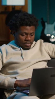 Neon ışıklarının altında uzaktan kumandalı bir dizüstü bilgisayarda çalışan, rahat bir dairedeki kanepede oturan dikey Afrikalı Amerikalı serbest yazar. Şık bir evde rahat bir adam modern üretkenliği ön plana çıkarıyor