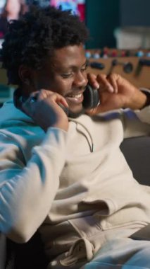 Dikey Video Afrikalı Amerikalı serbest çalışan adam internette geziniyor ve müzik dinliyor, modern evindeki şarkılarla eğleniyor. Genç yetişkin kanepede uzanıyor ve oturma odasında dinleniyor.