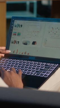 Vertical Video Afrikalı Amerikalı serbest çalışan, finansal grafikler kullanarak çalışan, istatistiksel verileri inceleyerek arz ve talep numaralarını karşılaştıran. Not defterine iş çizelgeleri ve yazılar kullanarak