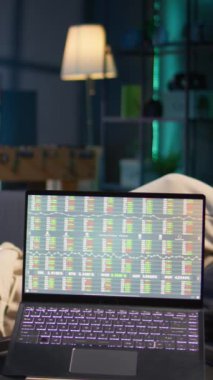 Dikey Videocu, bilgisayardan güncellenmeyi beklerken tablet üzerinde e-kitap okuyup müzik dinlerken borsa finansal rakamlarının güncellenmesini bekliyor. Ticari yatırım grafiklerini gösteren bilgisayarın yanındaki kişi