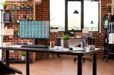 Finansal belgeleri gösteren bilgisayar ekranı başlangıç çalışma alanındaki geniş masanın üzerinde duruyor. Masaüstü bilgisayarı boş tuğla duvar odasındaki iş analizlerini gösteren bir ekranla ofis masasında..