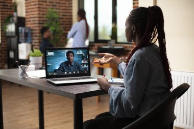 Siyahi kadın sanal toplantıda iş arkadaşıyla proje planlarını tartışarak uzaktan işbirliği yapmak için dizüstü bilgisayar kullanıyor. Masadaki kadın danışman pazarlama stratejilerini paylaşmak için erkek müşteriyle görüntülü görüşme yapıyor.