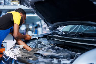Araç servisindeki BIPOC tamircisi hasarlı motoru değiştirdikten sonra fındıkları sıkmak için tork anahtarı kullanıyor. Çalışkan garaj çalışanı müşteri otomobilini tamir etmek için profesyonel araçlar kullanıyor