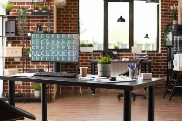 Finansal belgeleri gösteren bilgisayar ekranı başlangıç çalışma alanındaki geniş masanın üzerinde duruyor. Masaüstü bilgisayarı boş tuğla duvar odasındaki iş analizlerini gösteren bir ekranla ofis masasında..