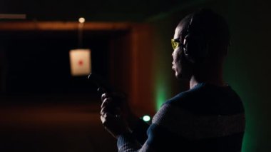 Mutlu atış poligonunun portresi. Müşteri silah dolduruyor, hedef vuruyor, eğleniyor. Zemin tesisinde neşeli bir adama yakın durun. Silah doldurun. Koruyucu gözlük takın.