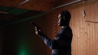 Atış talimi yapan gülümseyen bir adamın portresi, düzgün silah tutmayı ve eğlenmeyi öğrenmek. Neşeli silah meraklısı, silahlı, koruyucu gözlüklü, kamera A 'lı.