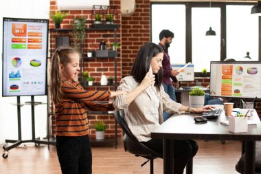 Bilgisayarı kullanan ve elinde telefon tutan genç bir kadın. Küçük bir kız başlangıç ofisinde sorun çıkarıyor. Kafkasyalı anne çoklu görev yapıyor, masaüstü bilgisayarı üzerinde çalışıyor ve kızı kollarını çekerken telefon görüşmesi yapıyor..