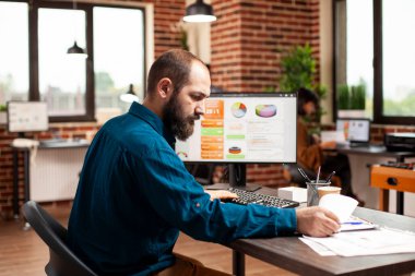 Masaüstü bilgisayarı iş analizlerini gösterirken, erkek çalışanlar mali evrakları gözden geçiriyorlar. Piyasa stratejisini araştırmakla meşgul bir işadamı ve başlangıç ofisindeki belgeler..