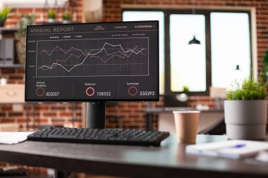 Şirket analitiği ve mali verilerini gösteren bilgisayar ekranı boş tuğla duvar ofisindeki modern masada duruyor. Masaya yerleştirilen kapalı bitki ve dosya dizinleri, profesyonel dokunuş ekle.