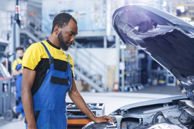 BIPOC araba servisi uzmanı bozuk motoru tamir etmek için profesyonel mekanik alet kullanıyor. Müşteri otomobili tamiri konusunda eğitimli uzman, optimal otomotiv performansı sağlıyor