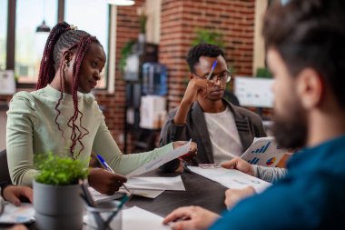 Afrika kökenli Amerikalı iş adamı ve kadının beyin fırtınası sırasında belgeleri incelemesine özen gösterin. Çok ırklı ekip üyeleri çizelge ve notlarla verimli bir tartışmaya giriştiler.