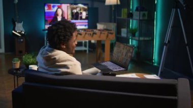 Kendine güvenen erkek konuşmacı, video konferans toplantısında meslektaşlarını selamlıyor, rahat bir çatı katında çevrimiçi uzaktan iletişimin tadını çıkarıyor. Genç siyahi yetişkin sanal tartışma sunuyor. Kamera B.