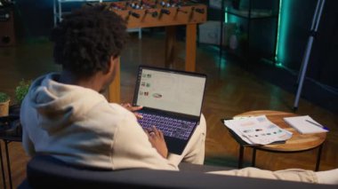 Evden çalışan Afrikalı bir Amerikalı bilgisayar ekranından istatistiksel verileri kontrol ediyor, finansal grafikleri analiz ediyor. Oturma odasındaki telgraf işçisi iş gelirlerini karşılaştırıyor. Kamera B.