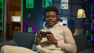 Afrika kökenli Amerikalı bir adam çatı katında video oyunu oynuyor, eğlence olsun diye kontrol cihazını tutuyor. Erkek oyuncu geceleri internet çok oyunculu oyunlara katılıyor. Kamera B.