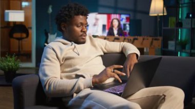 Pozitif Afro-Amerikan bir adam lüks bir çatı katında dizüstü bilgisayarda birden fazla iş yapıyor, serbest işini ve uzak sorumluluklarını yönetirken tamamen internete bağlı. Evde web taraması. Kamera B.