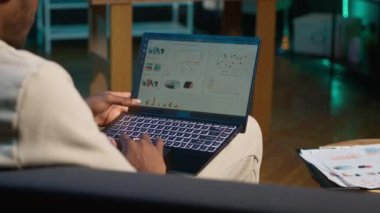 Finansal grafikler kullanarak evden çalışan Afrikalı Amerikalı serbest çalışan, arz ve talep sayılarını karşılaştırmak için istatistiksel verileri gözden geçiren. İş çizelgelerini kullanarak ve not defterine yazarak. Kamera A.