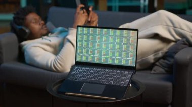 Müzikten hoşlanan ve tablet üzerinde e-kitap okuyan bir adam dizüstü bilgisayardan güncellenmesini beklerken borsa mali rakamlarının güncellenmesini bekliyor. Evinde, bilgisayarın yanında ticari yatırım grafikleri gösteren biri. Kamera A.