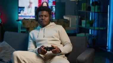 Evdeki kanepede oturan genç adam oyun konsolunda video oyunları oynayarak rahatlıyor, neon ışıklı apartman dairesinde internetteki çoklu oyuncu ve spor turnuvasında rekabet ederek gevşiyor. Kamera A.